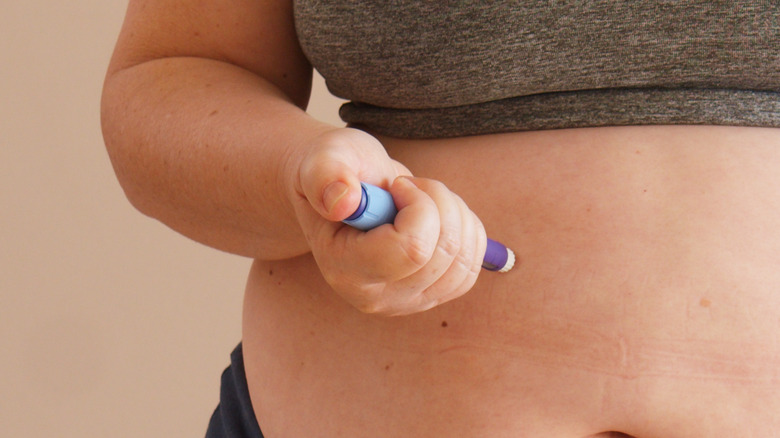 woman applying an injection to her stomach