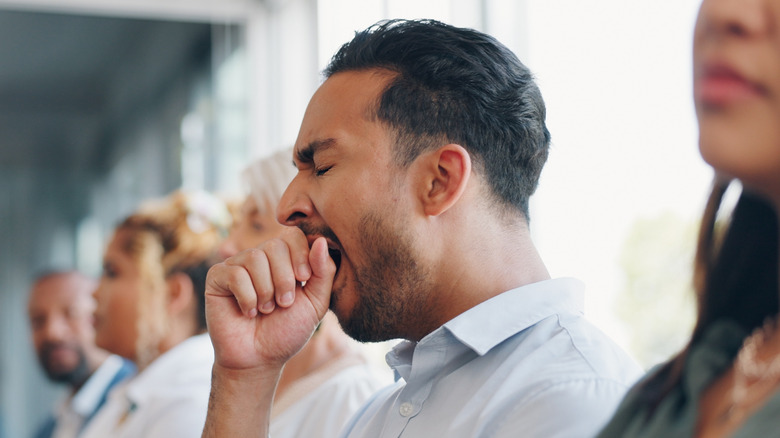 A man yawning inside a conference room