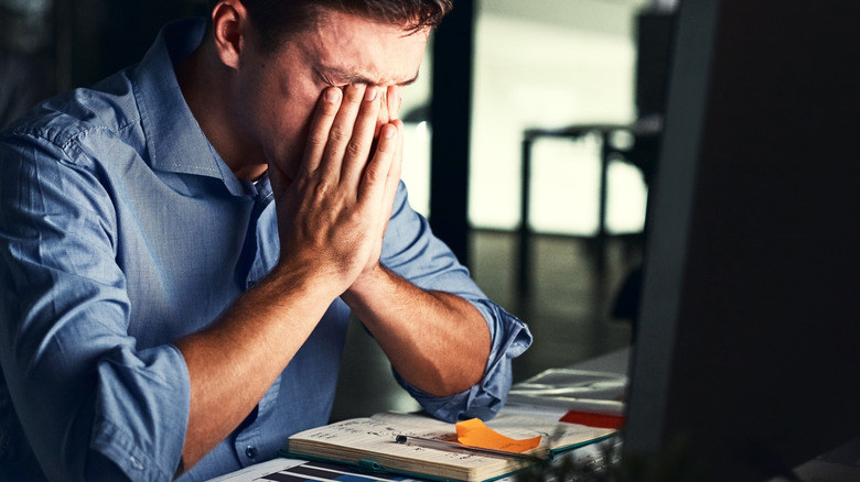 Stressed man rubbing eyes in front of computer monitor