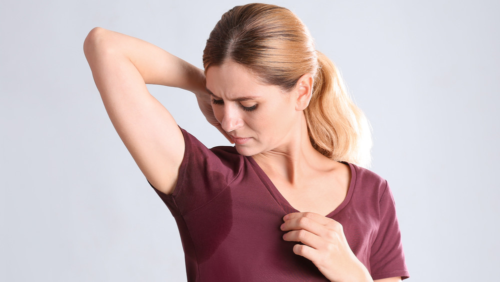 A woman with one arm up inspecting an under arm sweat stain