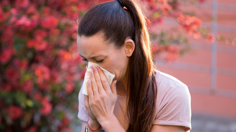 Woman sneezing into tissue in front of a tree