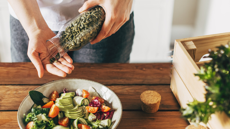 woman adding pumpkin seeds to a salad at home