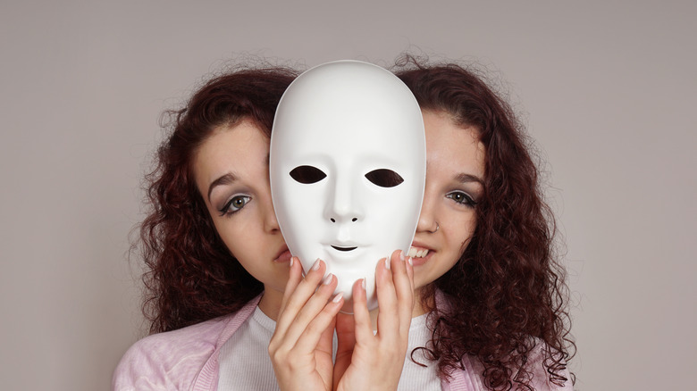 A woman smiling on one side of a mask and frowning on the other