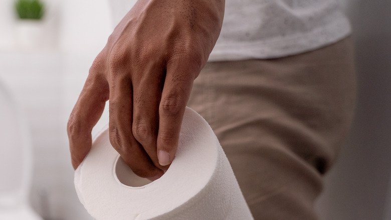 Man holding toilet paper entering bathroom