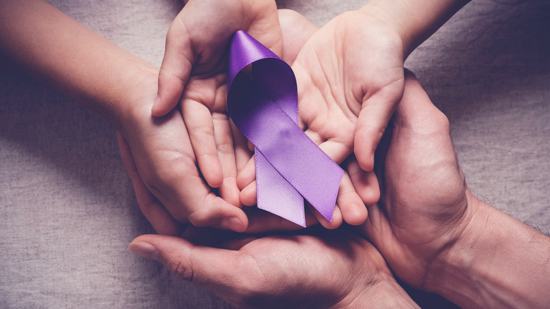 handles holding a purple ribbon that represents pancreatic cancer awareness 