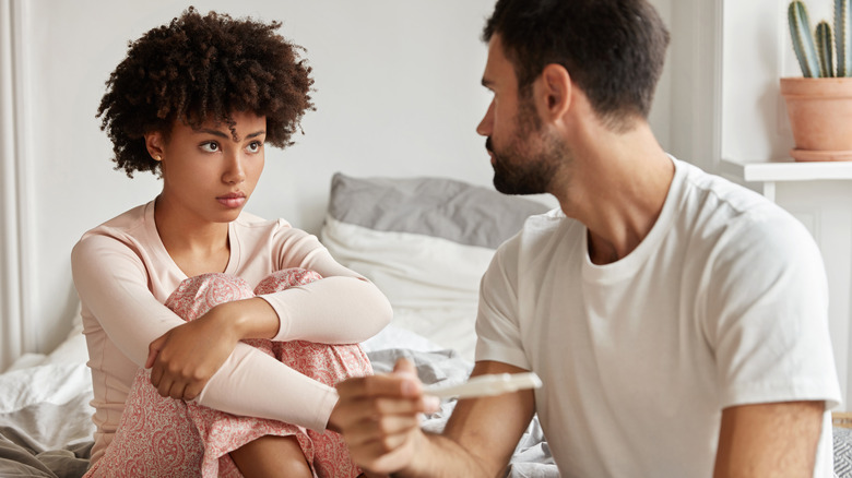 Couple sitting in bed looking upset, man holding a pregnancy test
