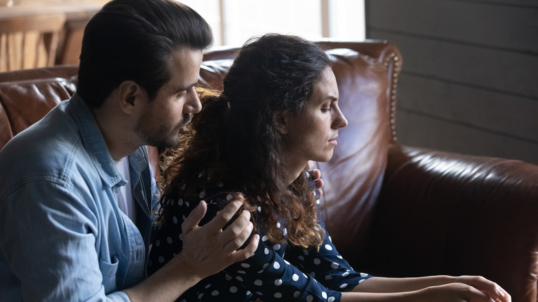 Man sitting behind his partner, holding her shoulders, supporting her