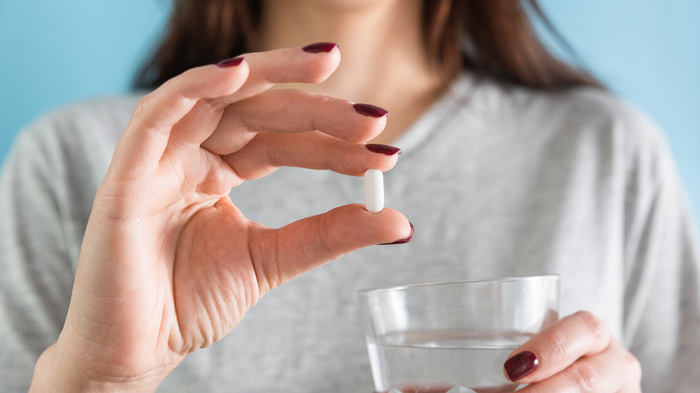 woman holding a statin in her hand that she is going to take with a glass of water