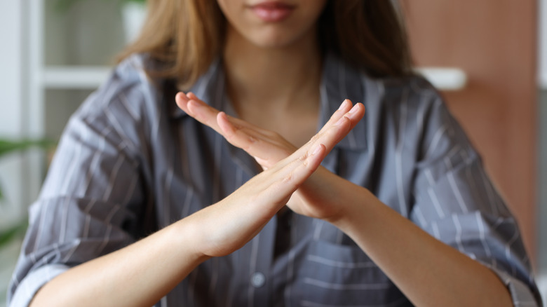 woman crossing her arms in the shape of an X while sitting at a table