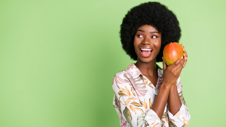 a person holding an unpeeled mango