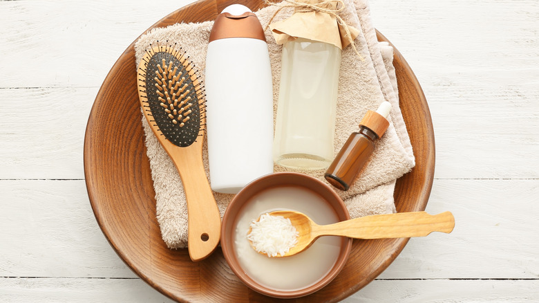 a brush, shampoo, a bottle and bowl of rice water, and an essential oil 