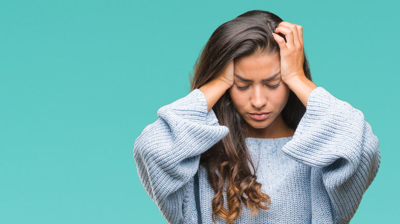 young woman in a blue sweater holding her head