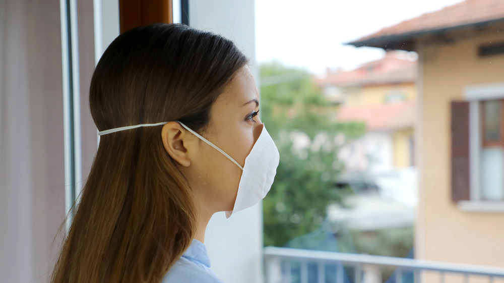 Woman with mask on looking out a window