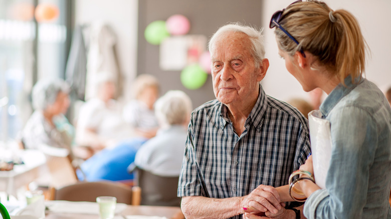 A senior man getting assistance from a young woman in a care facility