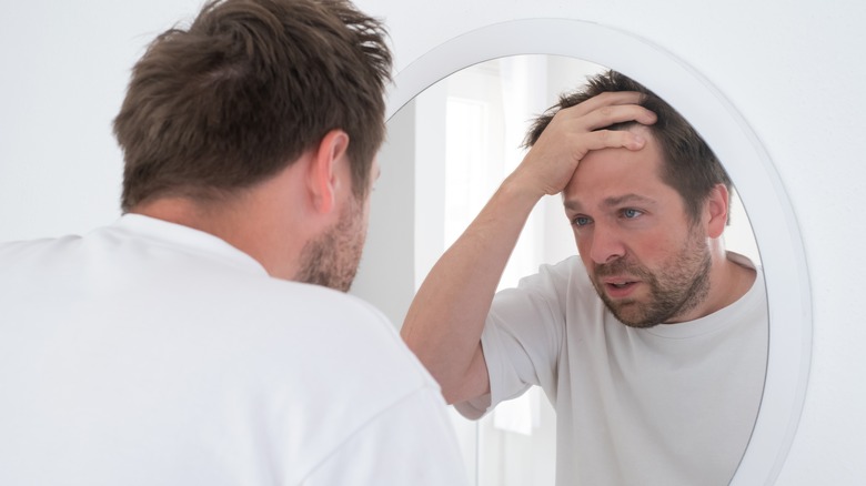 man holding head and looking in mirror