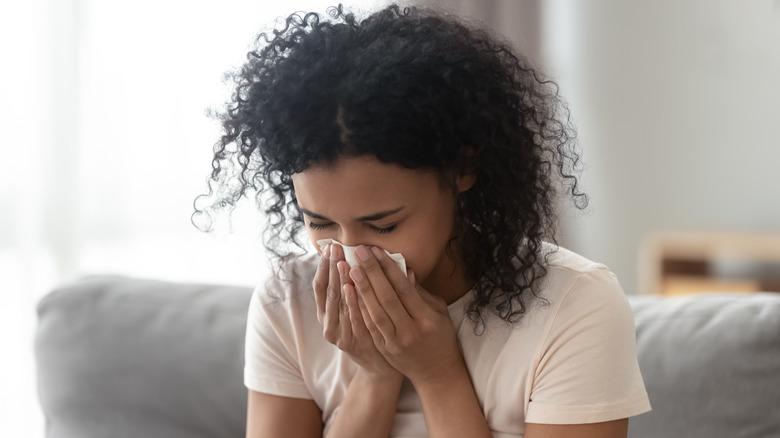 Woman blowing running nose with blanket wrapped around her