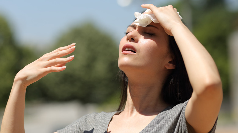 Woman standing in the sun, dabbing forehead sweat