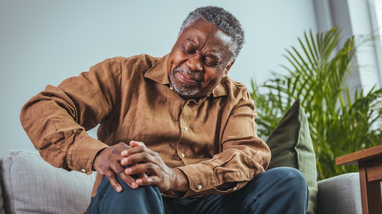 man wincing in pain while holding his foot