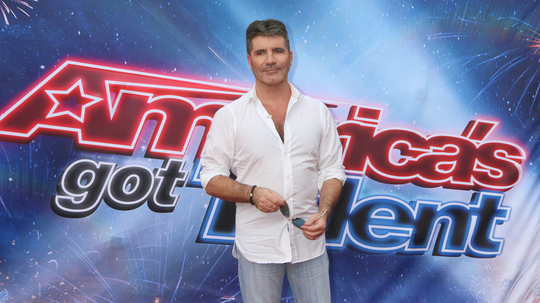 Simon Cowell stands in front of a sign that reads "America's Got Talent"