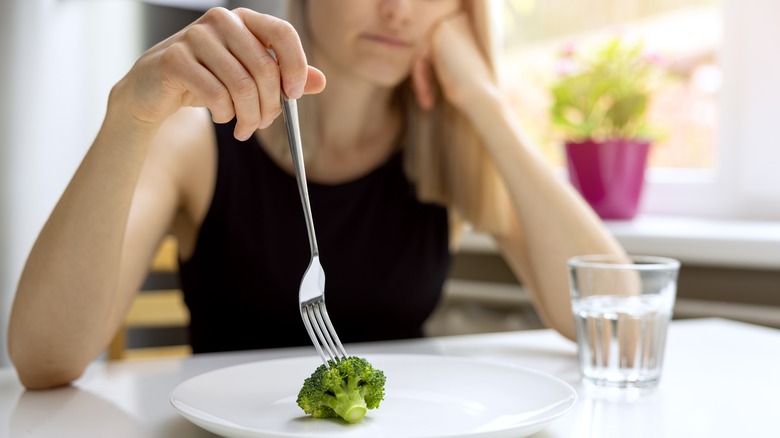 unhappy woman picking at broccoli on plate