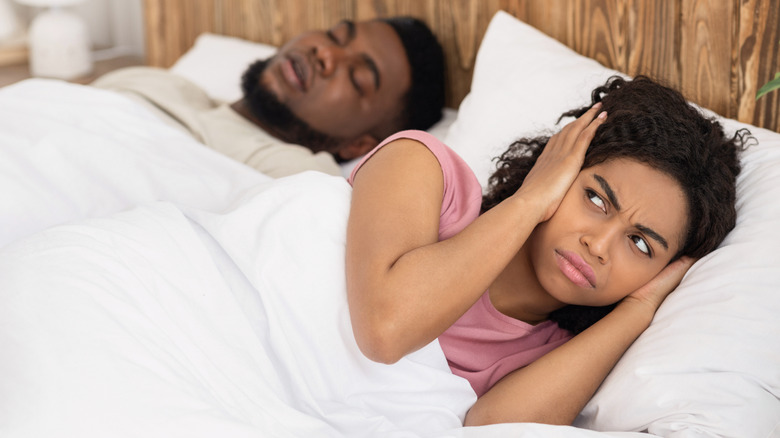 Woman covering ears while man snores