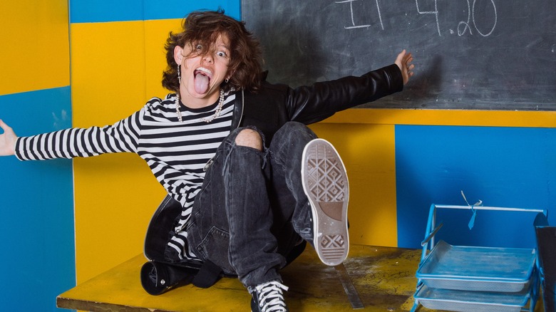 Jacob Sartorius sitting in front of a chalkboard and a blue and yellow wall making a silly face