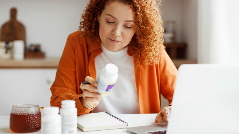 woman looking at supplement and checking on laptop