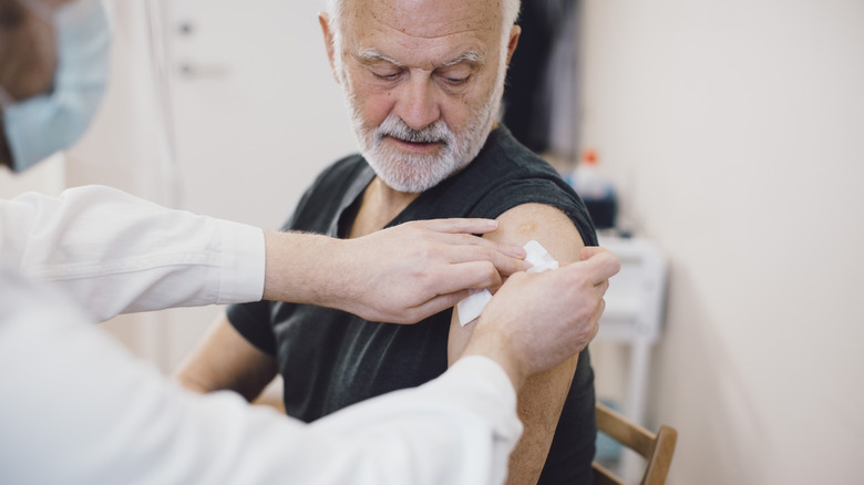An older man getting a bandage after an injection in his arm