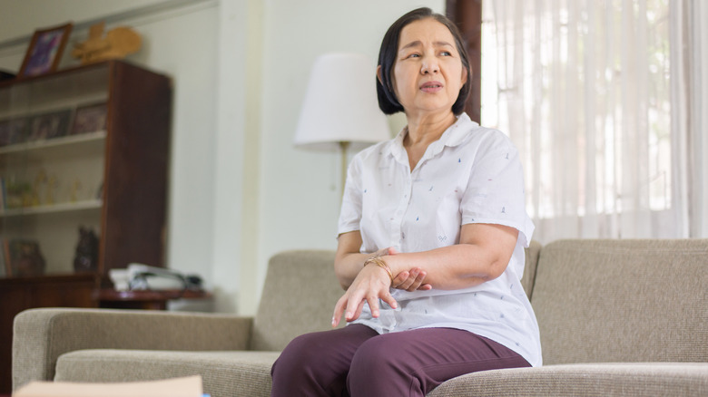 Woman with Parkinson's grasping her wrist on couch