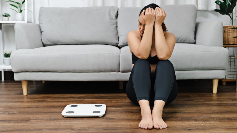 Woman sitting on the floor and looking at the scale