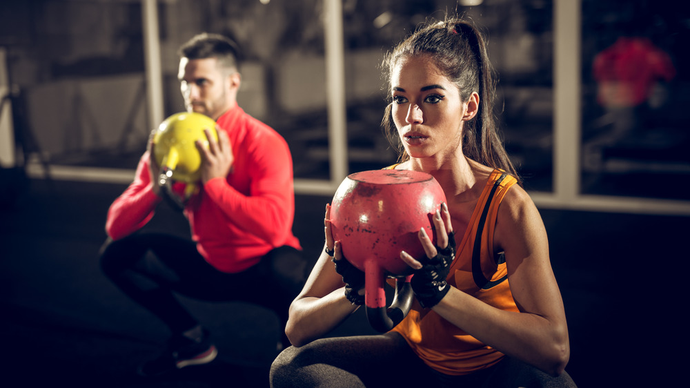 A couple doing kettlebell squats in a gym at night