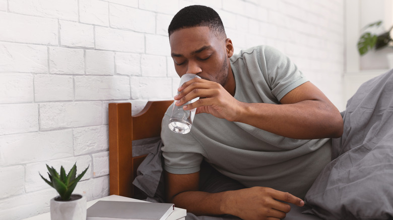 Black man drinking water from bed