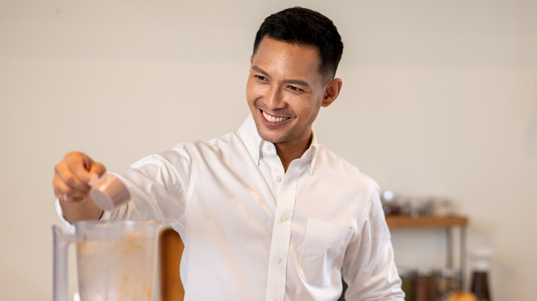 A man adding a scoop of protein powder to a blender
