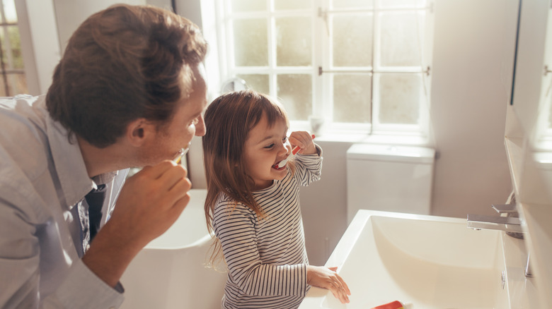 Man and little girl brushing their teeth in mirror 