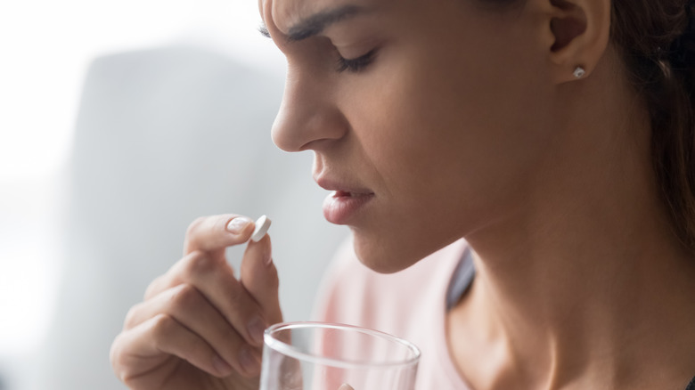 Woman hesitating taking ibuprofen tablet