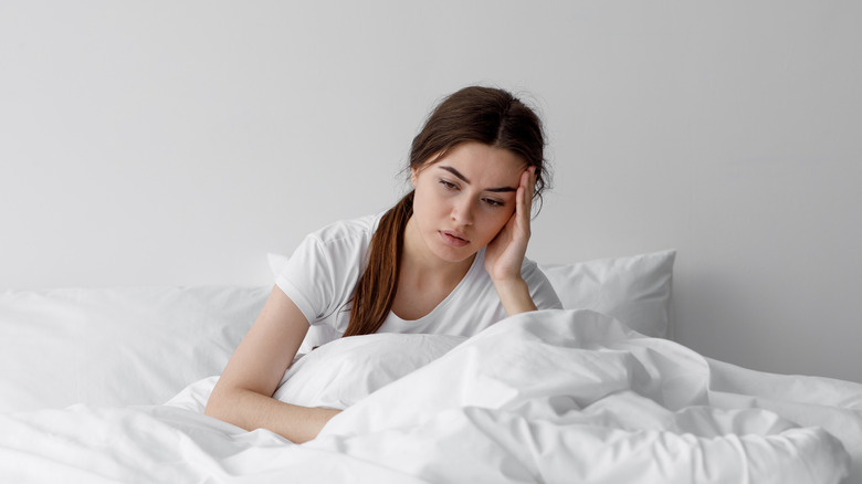 A woman sitting up in bed and holding her head