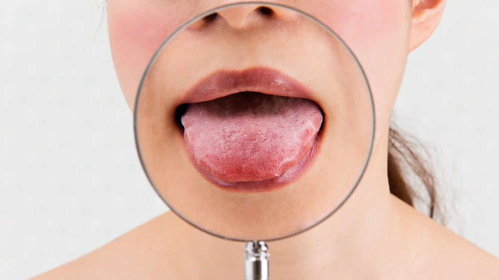 A woman using a magnifying glass to show off her tongue 