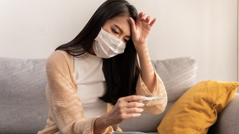 Masked woman holding thermometer 