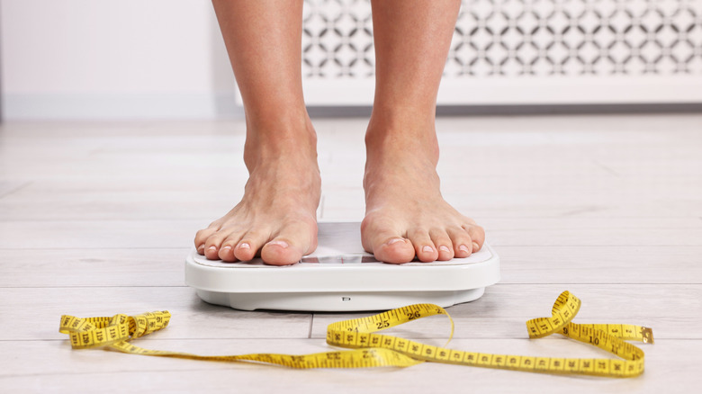 female feet on scale with tape measure on floor