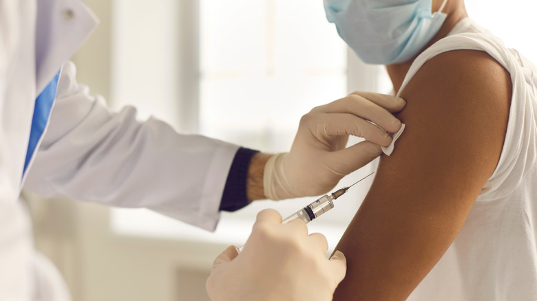 Close up of masked person receiving COVID-19 vaccine in arm