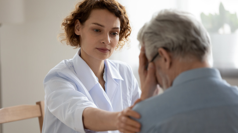 Doctor placing comforting hand on older patient's shoulder who is holding his head