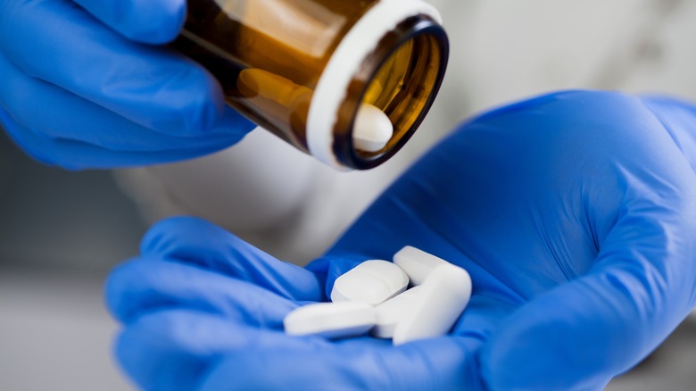 Close up of medical worker's hands wearing blue latex protective gloves pouring white pills into palm