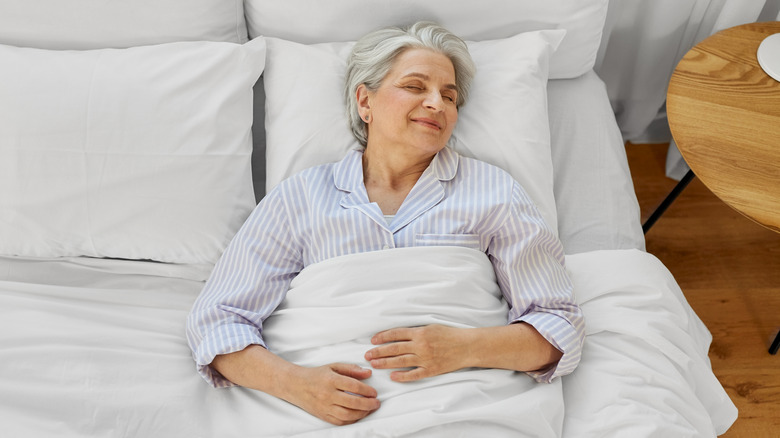 Older woman with gray hair smiling asleep in bed