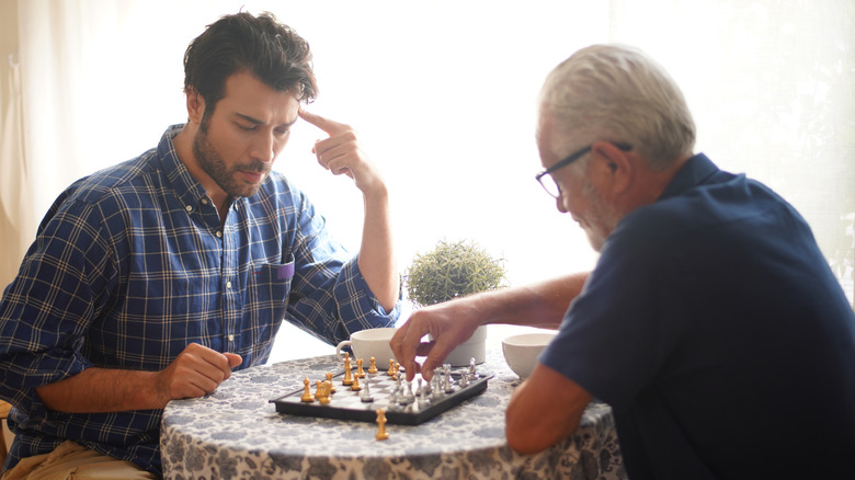 younger man playing chess with older man at table