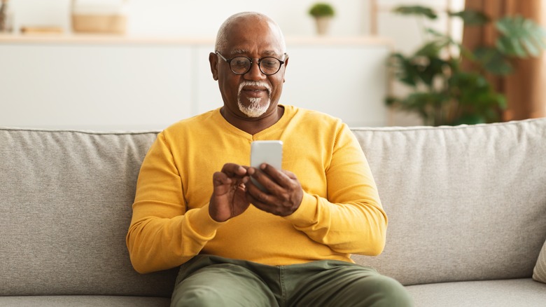 Older man sitting on sofa using smart phone