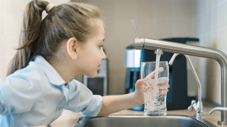 young girl filling a glass of water from the tap