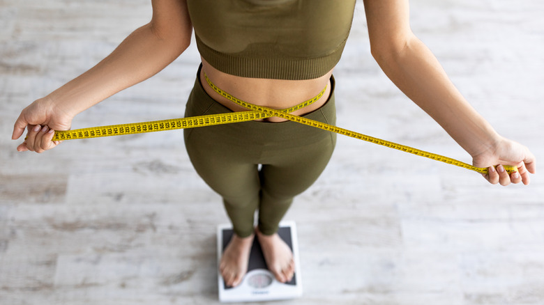 woman standing on a scale while measuring her waist