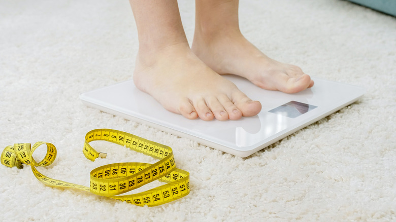 Person standing on scale next to tape measure