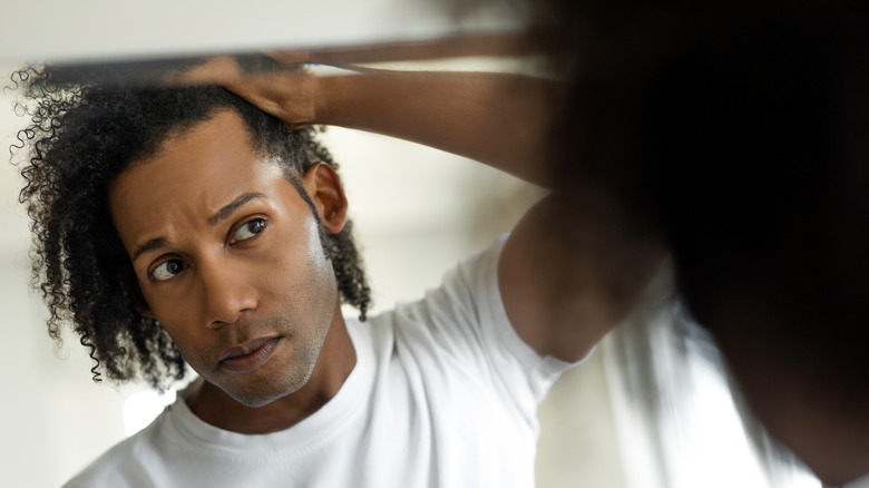 Man examining hair in mirror