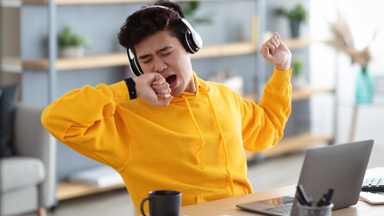 a teenage boy yawning at his computer